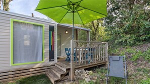 Una casa móvil con porche, mobiliario exterior y una sombrilla verde.