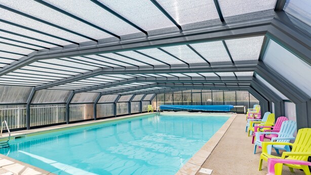 Une piscine intérieure dotée d’un toit en verre, entourée de fauteuils colorés.