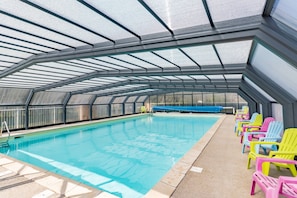 Une piscine intérieure dotée d’un toit en verre, entourée de fauteuils colorés.