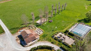 Vue aérienne d’une propriété comprenant un grand champ verdoyant, un bâtiment avec un toit en tuiles et une piscine.