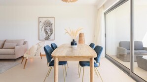 Ein modernes Wohnzimmer mit einem Holzesstisch, blauen Stühlen, einem weißen Sofa, einem großen Fenster und einer Deckenleuchte.