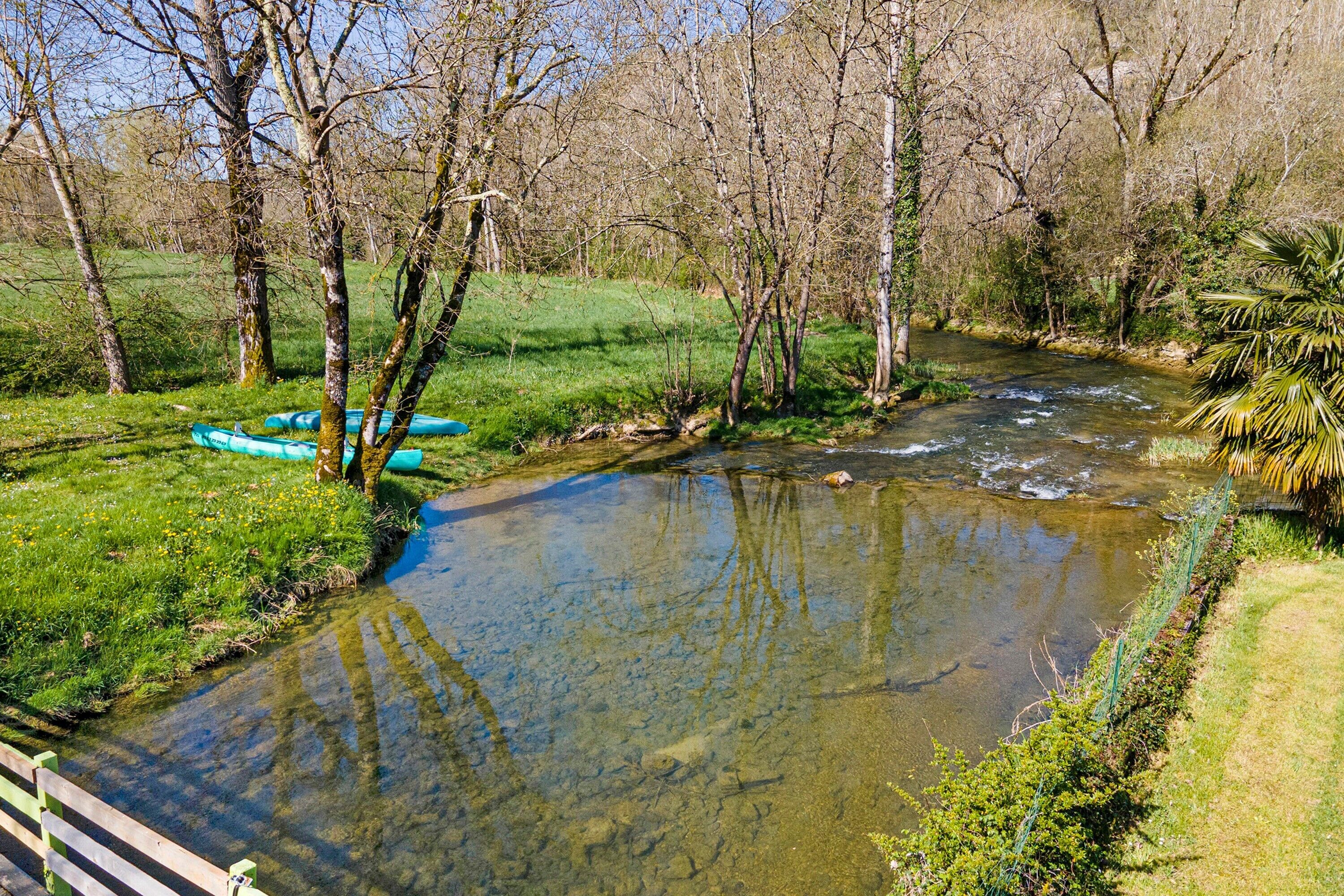 A river with kayaks, surrounded by trees and grass.
