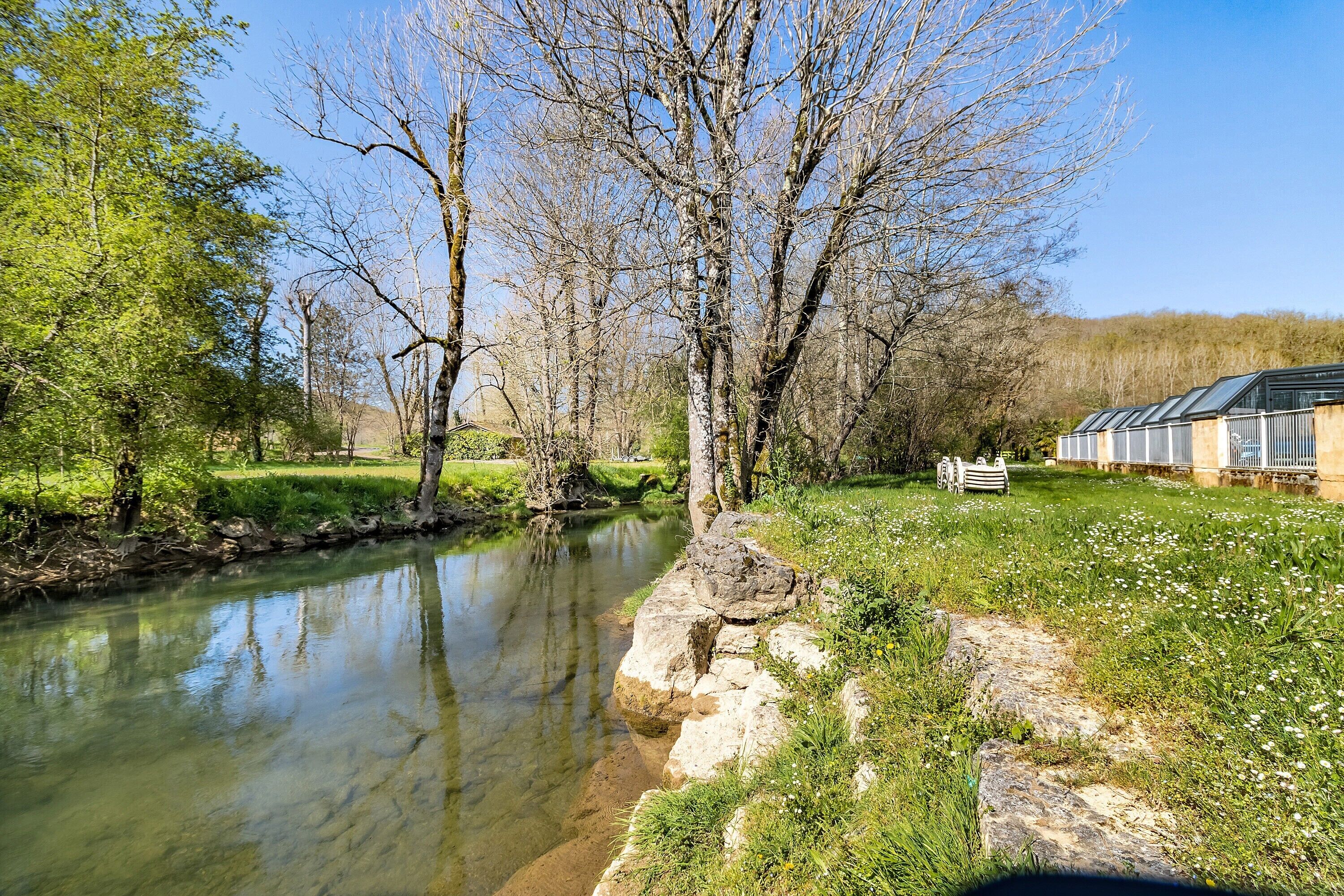 A river with clear water, surrounded by trees and a grassy area.