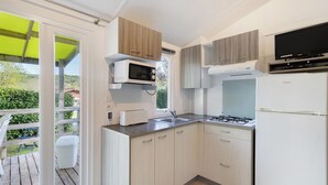 Cocina compacta con microondas, estufa y lavamanos, armarios de madera y un televisor.