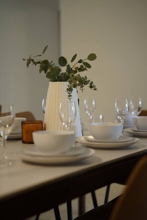 A dining table set with white plates, bowls, and wine glasses, with a white vase containing green foliage in the center. - Modern 5BR Family Retreat Comfort in Calamvale (Calamvale)