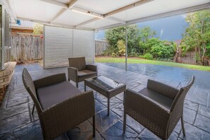 An outdoor patio with wicker furniture, a glass table, and a view of the backyard.