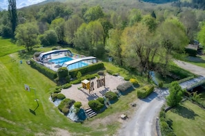 Ein modernes Haus mit Schwimmbecken, umgeben von üppigem Grün und einer kleinen Brücke.