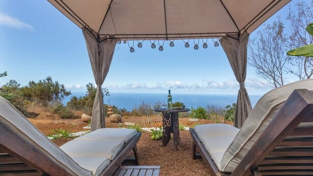 A covered outdoor seating area with two lounge chairs and a table, overlooking a scenic view of the sea. - Charming Farmhouse Retreat in Santa Ursula, Tenerife (santa ursula)