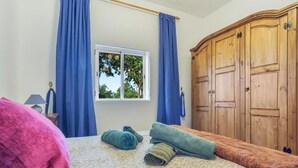 A bedroom with a bed, blue curtains, a wooden wardrobe, and a window with a view of trees. - Charming Farmhouse Retreat in Santa Ursula, Tenerife (santa ursula)