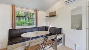 Ein gemütlicher Raum mit eingebautem Sitz- und Esstisch, einem fensterbelaubten Fenster, einem Spiegel und einer Klimaanlage.