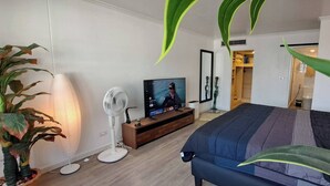 Ein Schlafzimmer mit Bett, Fernseher, Ventilator und Pflanze.