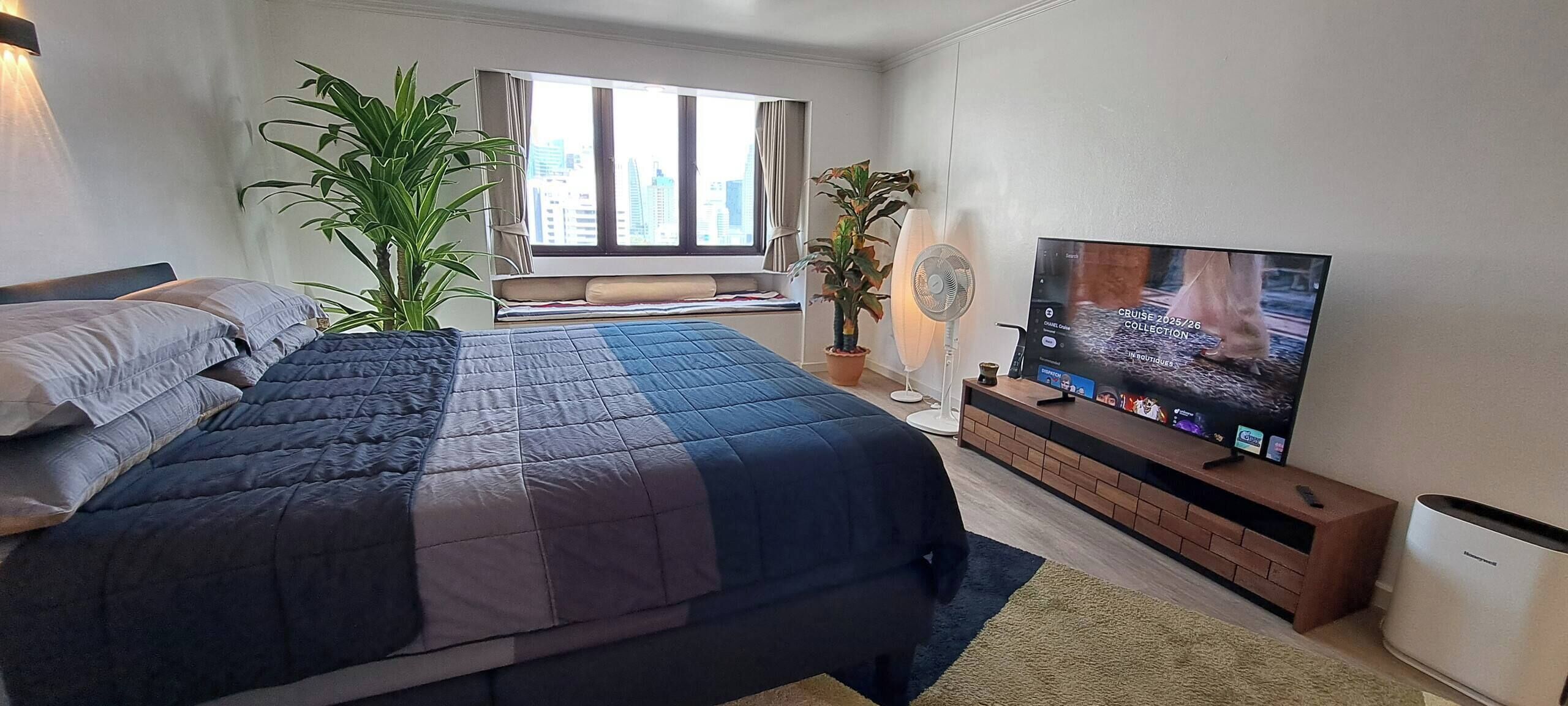 A bedroom with a bed, a TV, and two potted plants.