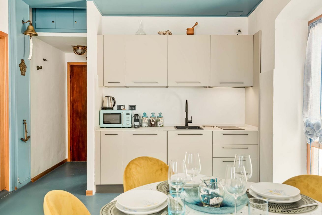 Une cuisine compacte avec des meubles blancs, un four à micro-ondes et un évier. On y trouve une table à manger, mise avec des assiettes et des verres.