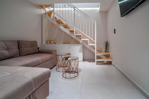 A modern living room with a sofa, a small table, and a staircase with wooden steps. - Pothos Luxury Maisonette (Iraklio)