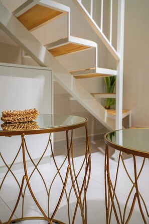A modern interior with a staircase, two round tables with gold wire legs, and a woven basket on one table. - Pothos Luxury Maisonette (Iraklio)