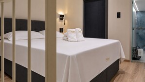 Een hotelkamer met een bed, een wandlamp, een deur en een handdoekrek met handdoeken.