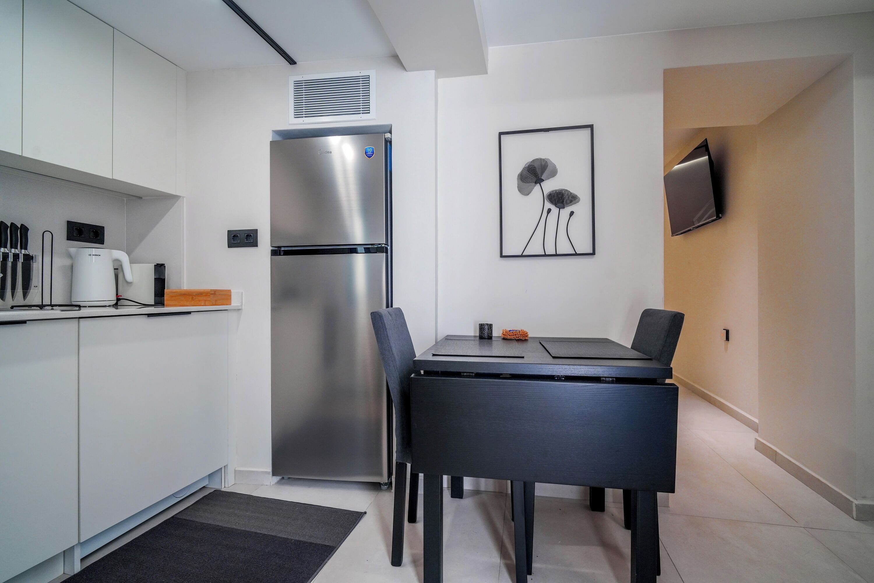 Una cucina funzionale con frigorifero integrato, un'area pranzo con tavolo e sedie, e una TV a schermo piatto montata a parete.