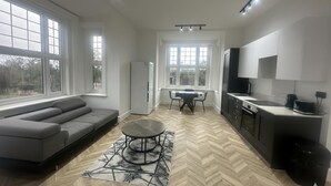 A modern kitchen with a dining area, large windows, and a grey sofa.