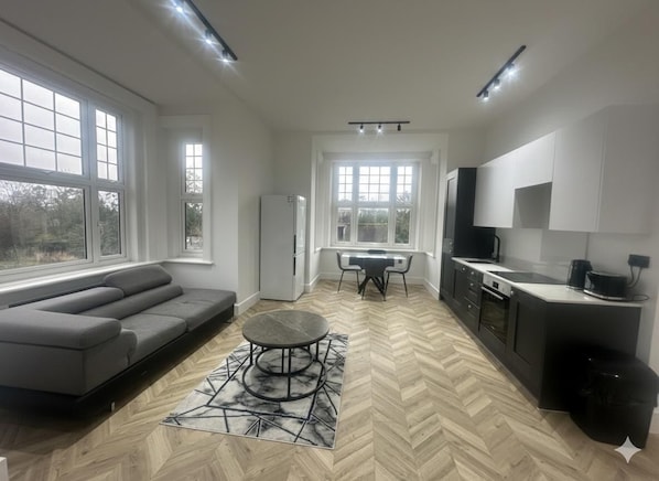Eine moderne Küche mit Essbereich, großen Fenstern und einem grauen Sofa.