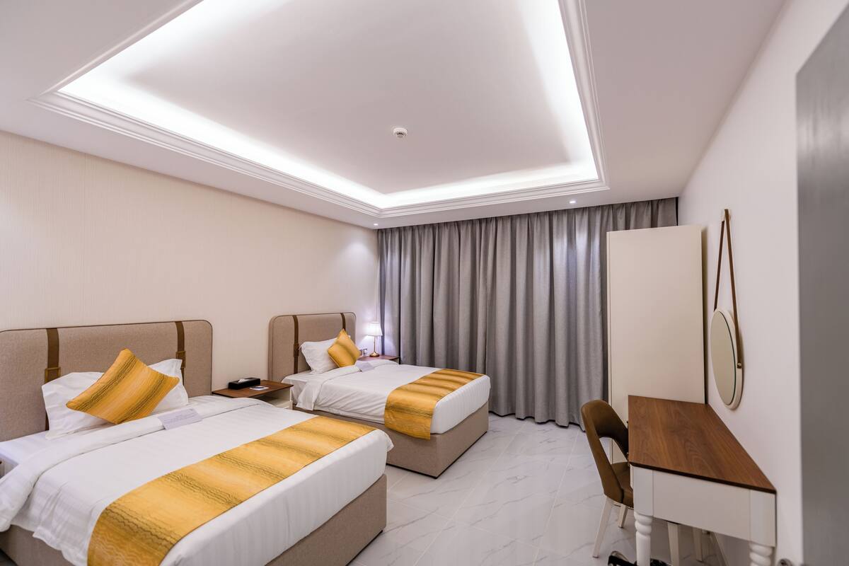 Habitación de hotel con dos camas, un escritorio, una silla, un espejo y una ventana con cortinas.