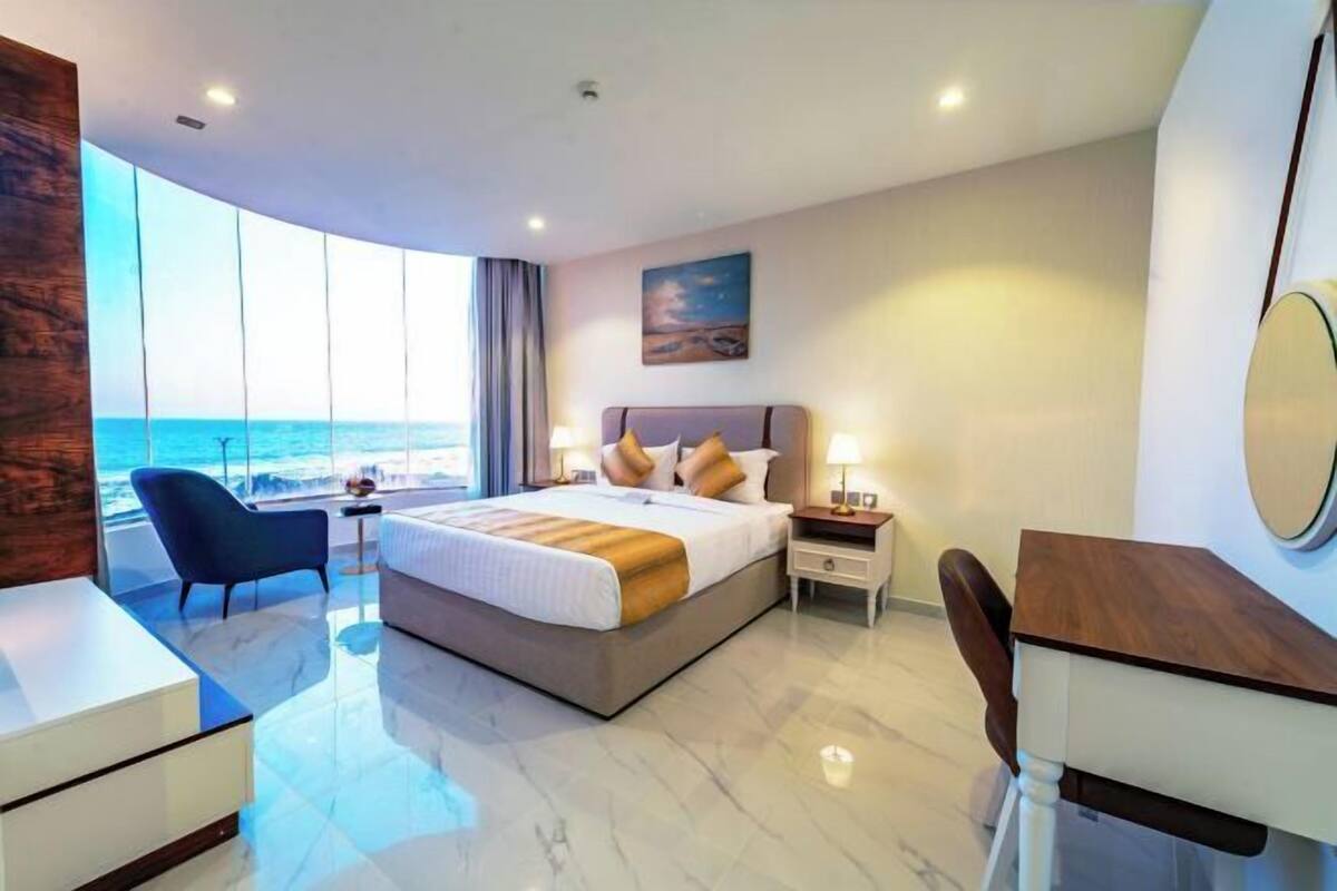 Una habitación de hotel moderna con una cama grande, un escritorio, una silla y vistas al océano.