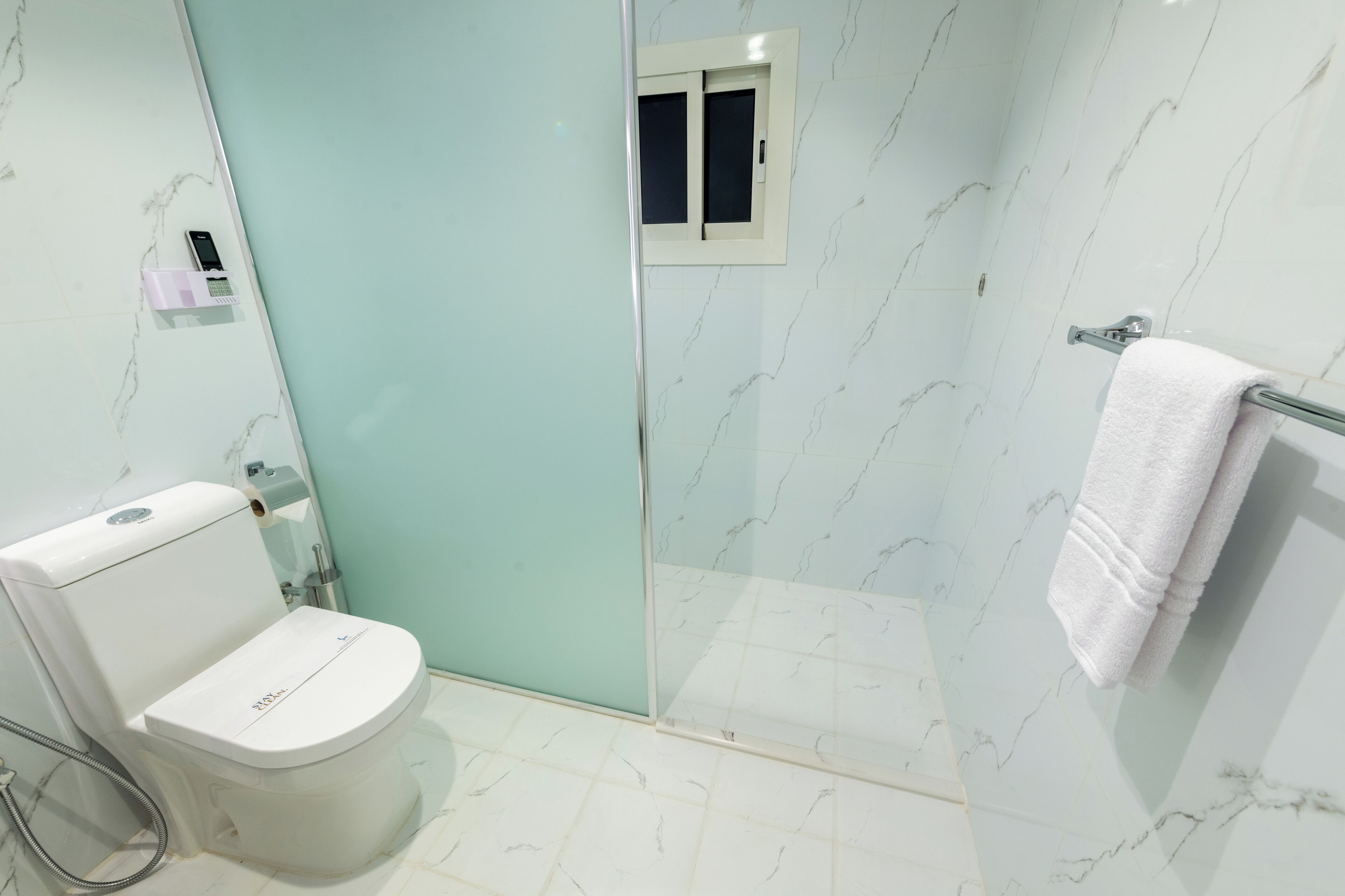 A bathroom with a toilet, a glass shower enclosure, a towel rack, and a marble-patterned wall.