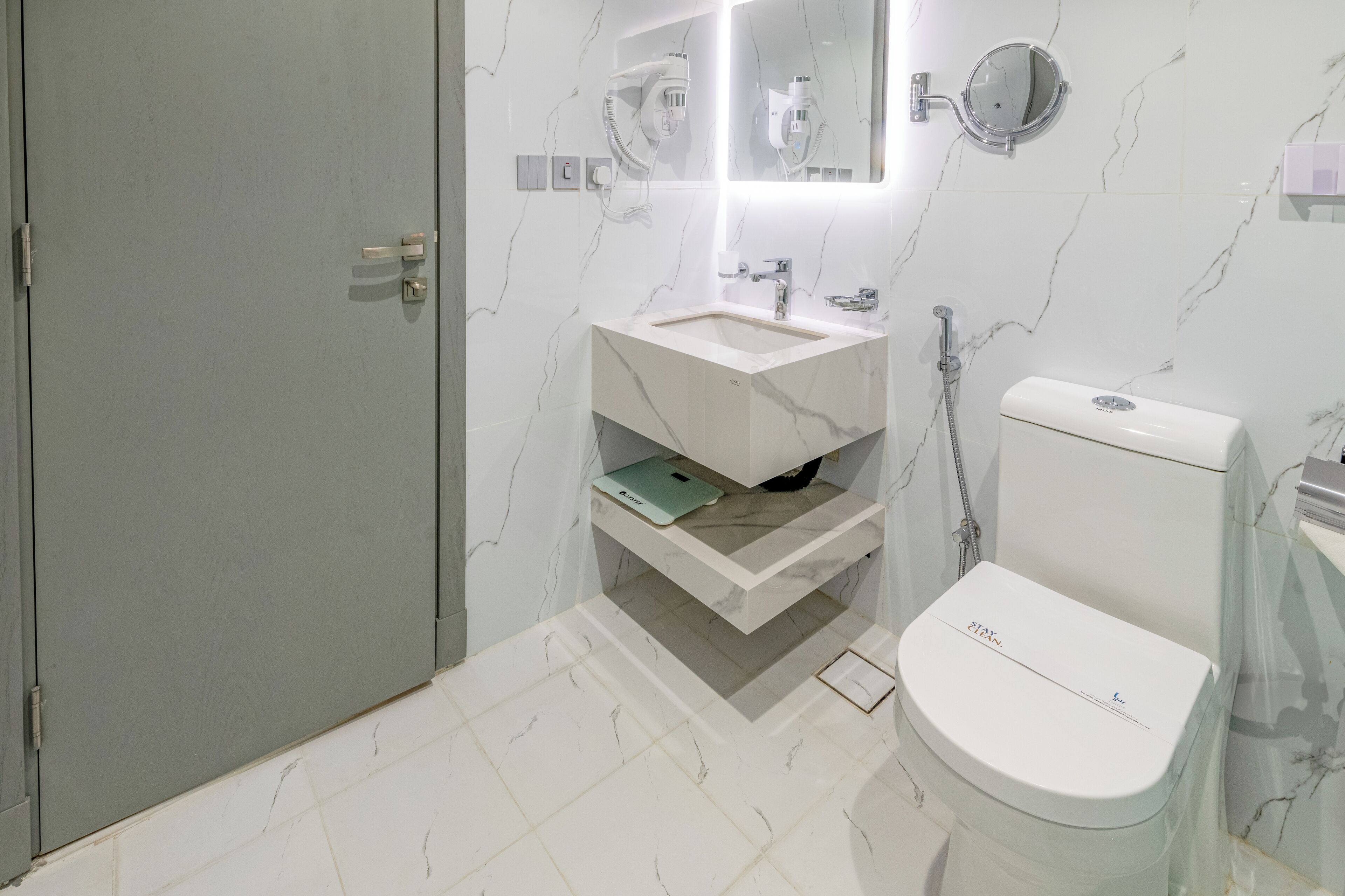 Un baño con piso de mármol, inodoro blanco, lavamanos con espejo y ducha.