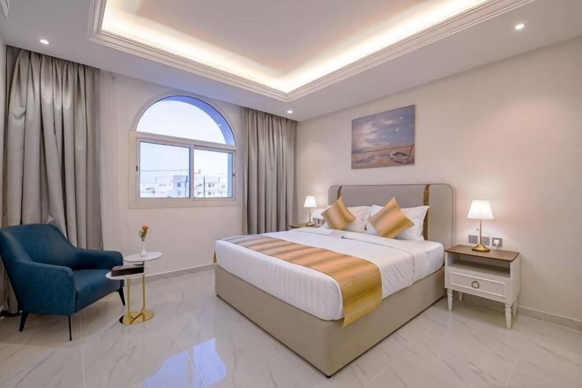 Habitación de hotel con una cama grande, un escritorio, una silla, una mesita de noche y una ventana con cortinas.