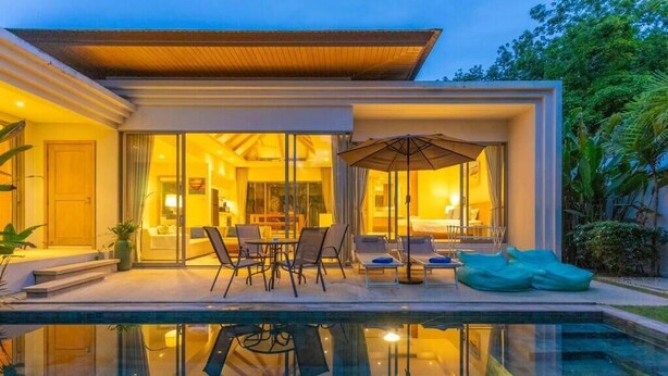 Una casa moderna con un patio de cristal, piscina y mobiliario exterior.