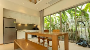 Una cocina moderna con armarios blancos, un refrigerador de acero inoxidable y un comedor con mesa y banco de madera.
