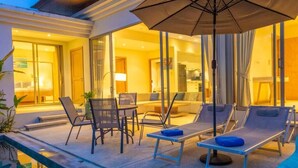 Zona junto a la piscina con sillones, una mesa y una sombrilla.