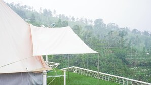 A tent with a white canopy and a rope ladder, set against a backdrop of a green hillside with trees. - Sun CampGround (Garung)