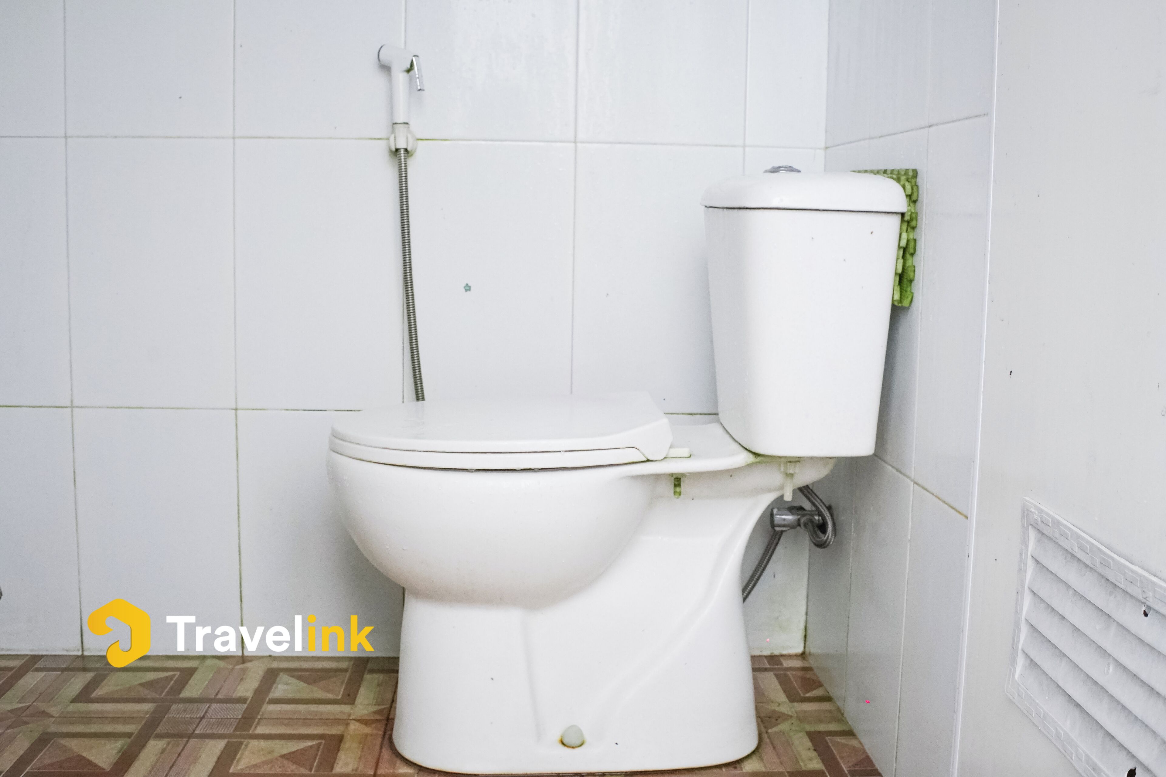 A white toilet with a shower attachment in a bathroom with tiled walls and patterned floor.