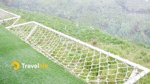 A rope net bridge over a grassy area with a hilly landscape in the background. - Sun CampGround (Garung)