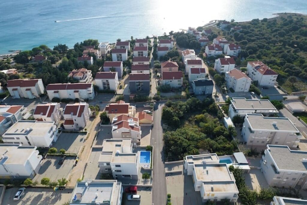 An aerial view of a coastal residential area with white buildings, red roofs, and a clear view of the sea.