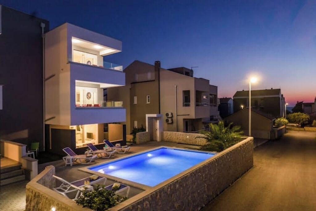 Un bâtiment moderne à deux étages, doté d’une piscine et de chaises longues.