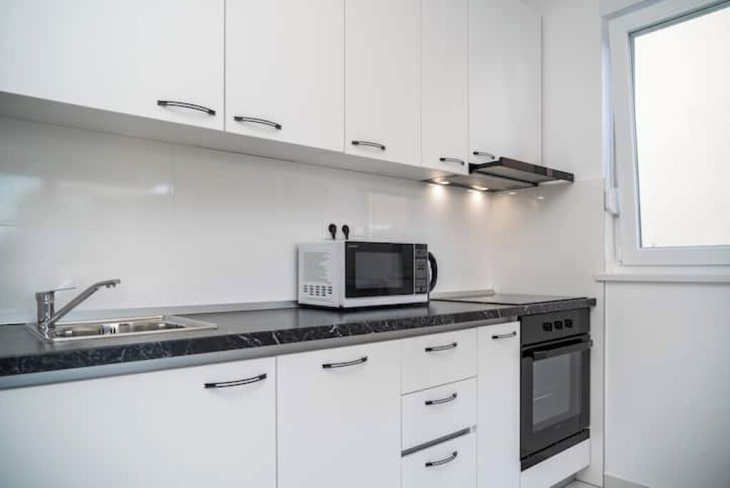 A modern kitchen with white cabinets, a black countertop, a microwave, a sink, and an oven.