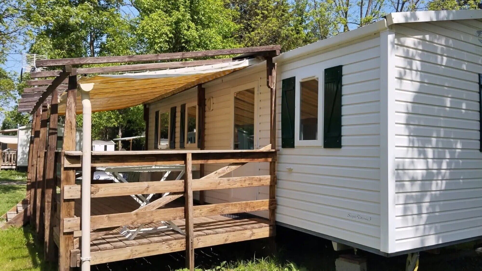 A mobile home with a wooden deck, a covered porch, and a window.