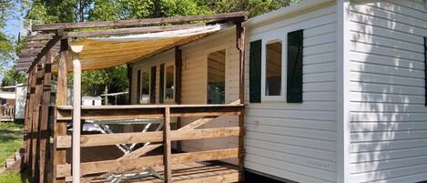 A mobile home with a wooden deck, a covered porch, and a window.