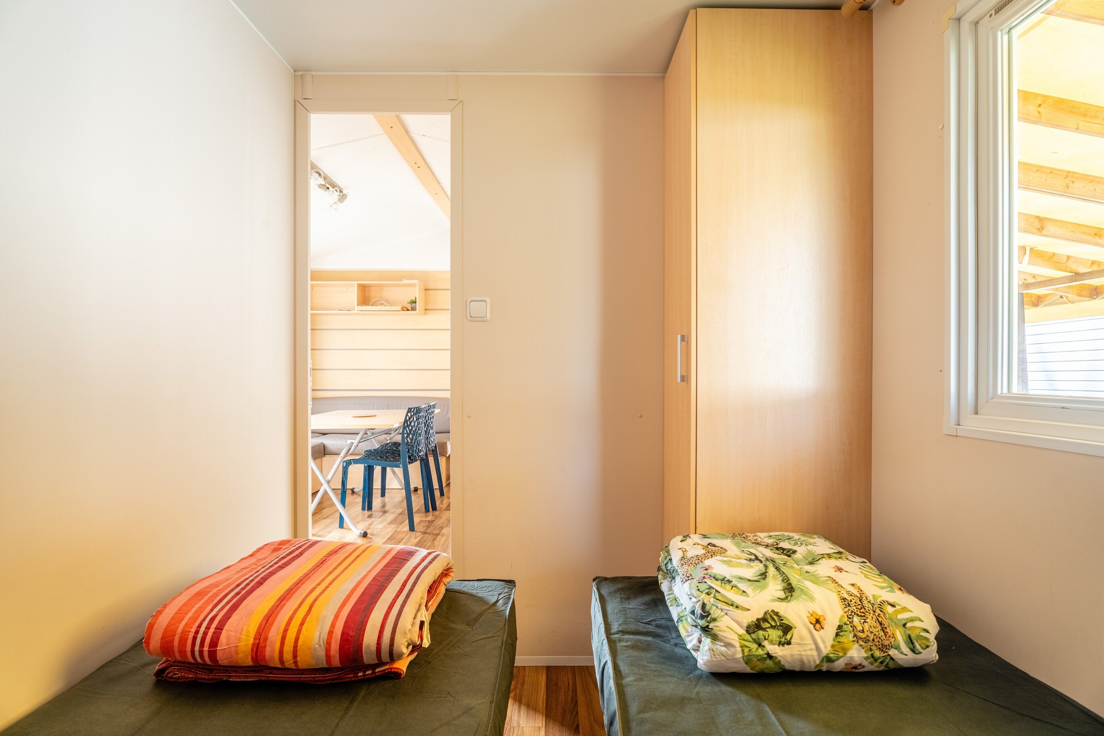 Habitació petita amb dos llits, un armari de fusta, una finestra i una porta que dona a un balcó.