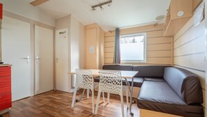 Una habitación compacta con piso de madera, un sofá marrón, una mesa blanca con sillas y una ventana con vistas.