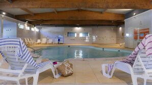Una piscina interior con sillones de descanso y un techo con vigas a la vista.