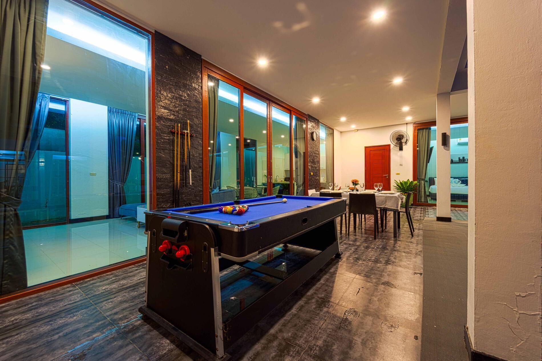 A pool table in a well-lit room with a view of a balcony and a dining area.
