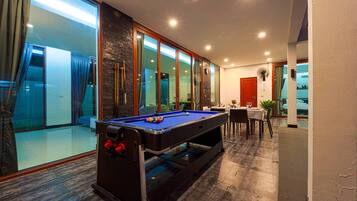 A pool table in a well-lit room with a view of a balcony and a dining area.