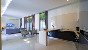 A modern kitchen with a central island, a dining area with chairs, and a TV mounted on the wall. - Beautiful 4-Bedroom Pool Villa BL9 (Hua Hin)