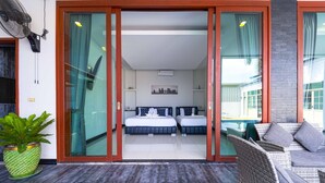 A modern hotel room with a sliding glass door leading to a balcony. The room has two beds, a small table, and a potted plant. - Beautiful 4-Bedroom Pool Villa BL9 (Hua Hin)