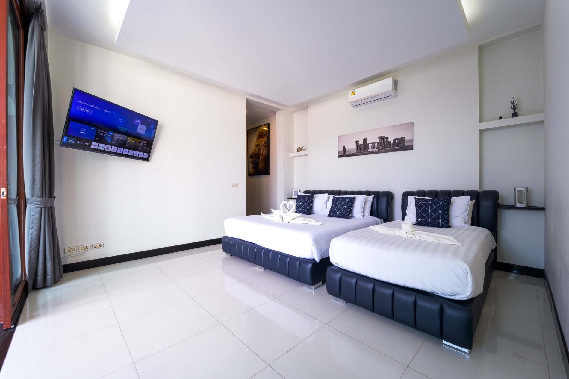 A modern hotel room with two beds, a flat-screen TV mounted on the wall, and a cityscape painting above the bed.