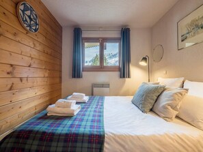 A hotel room with a wooden wall, a bed with white linens, a plaid blanket, and a window with curtains. - Close to Ski Piste Prarion - Swimming pool & Gym (Les Houches)