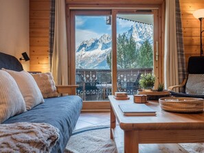 Una habitación acogedora con una cama, una mesa de madera y vistas a montañas a través de un ventanal grande.