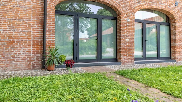 Un edificio de ladrillo con grandes puertas de vidrio y un pequeño jardín con plantas en macetas.